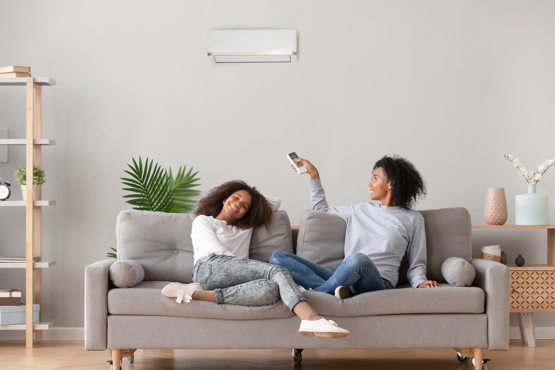 Happy family relax on sofa under air conditioner,mom holding remote control switch on conditioning in living room adjust comfort temperature for daughter, climate system at modern home