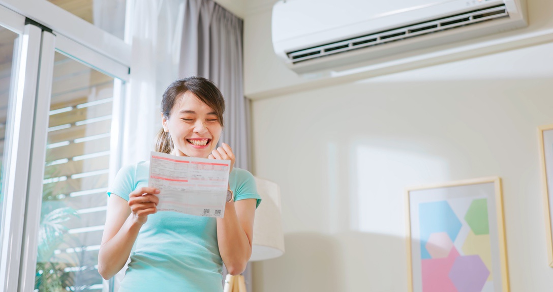 Smiling homeowner holding cooling bill underneath ductless mini split AC